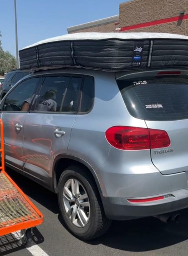 A couple waits as their old mattress, strapped to the top of their car, is taken to the back of a Costco store for return