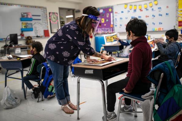 Teacher Elizabeth DeSantis, wearing a mask and face shield, helps a first grader during reading class at Stark Elementary School.